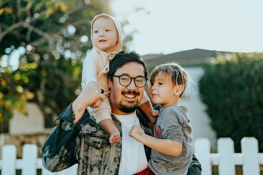 A father smiling and holding his two young children outdoors