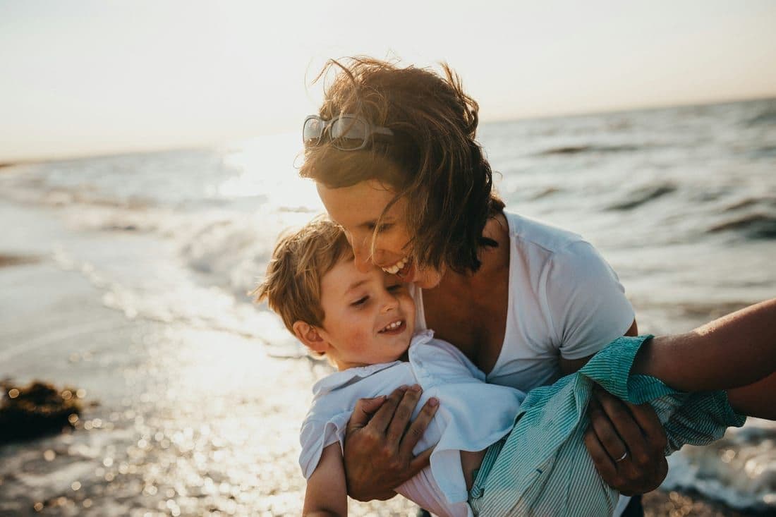 A parent holding their laughing child at a sunlit beach