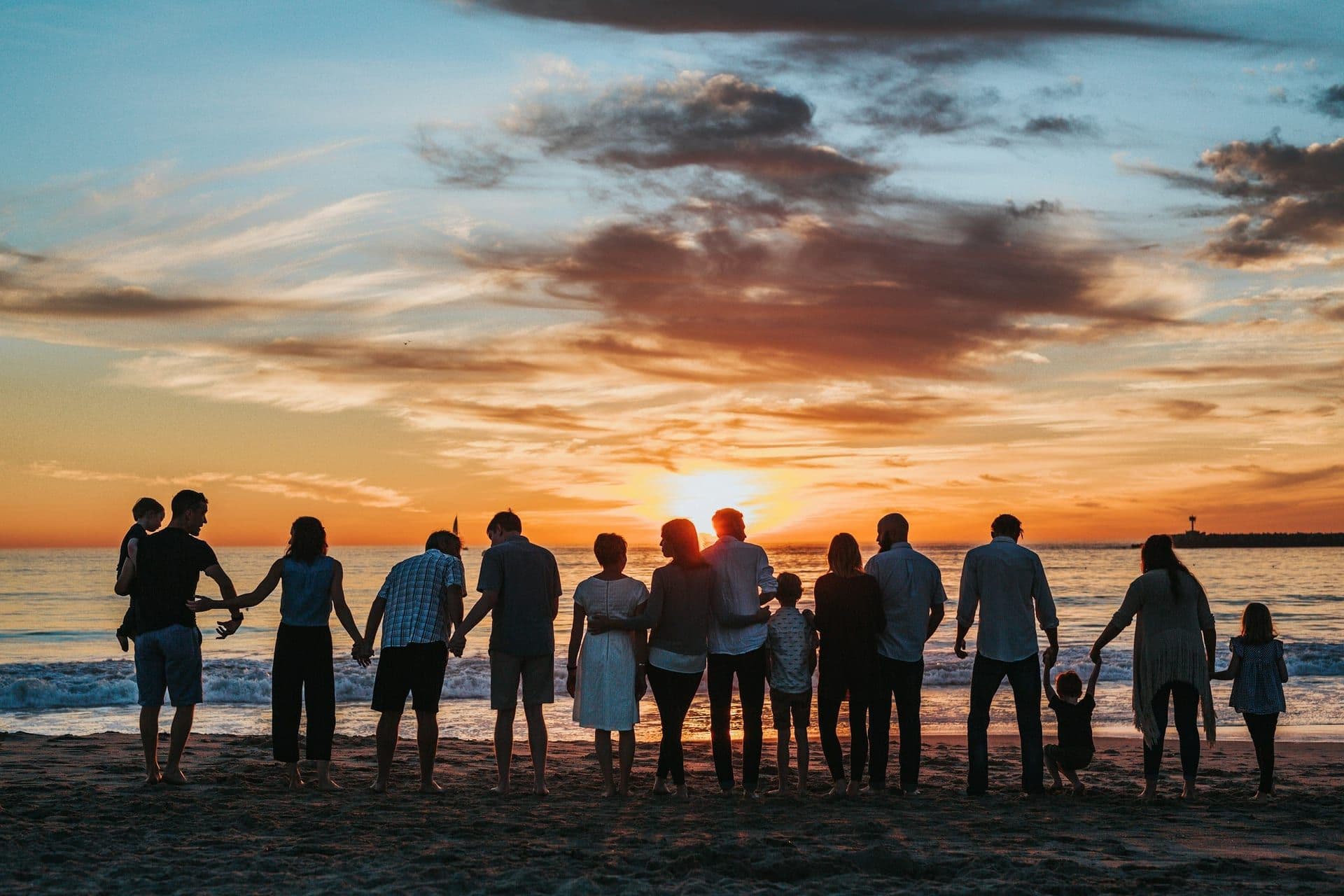 A multi-generational family holding hands at a coastal sunset
